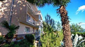 A multi-story building with balconies, surrounded by lush greenery and palm trees. - Apartment Visnja (Rijeka)