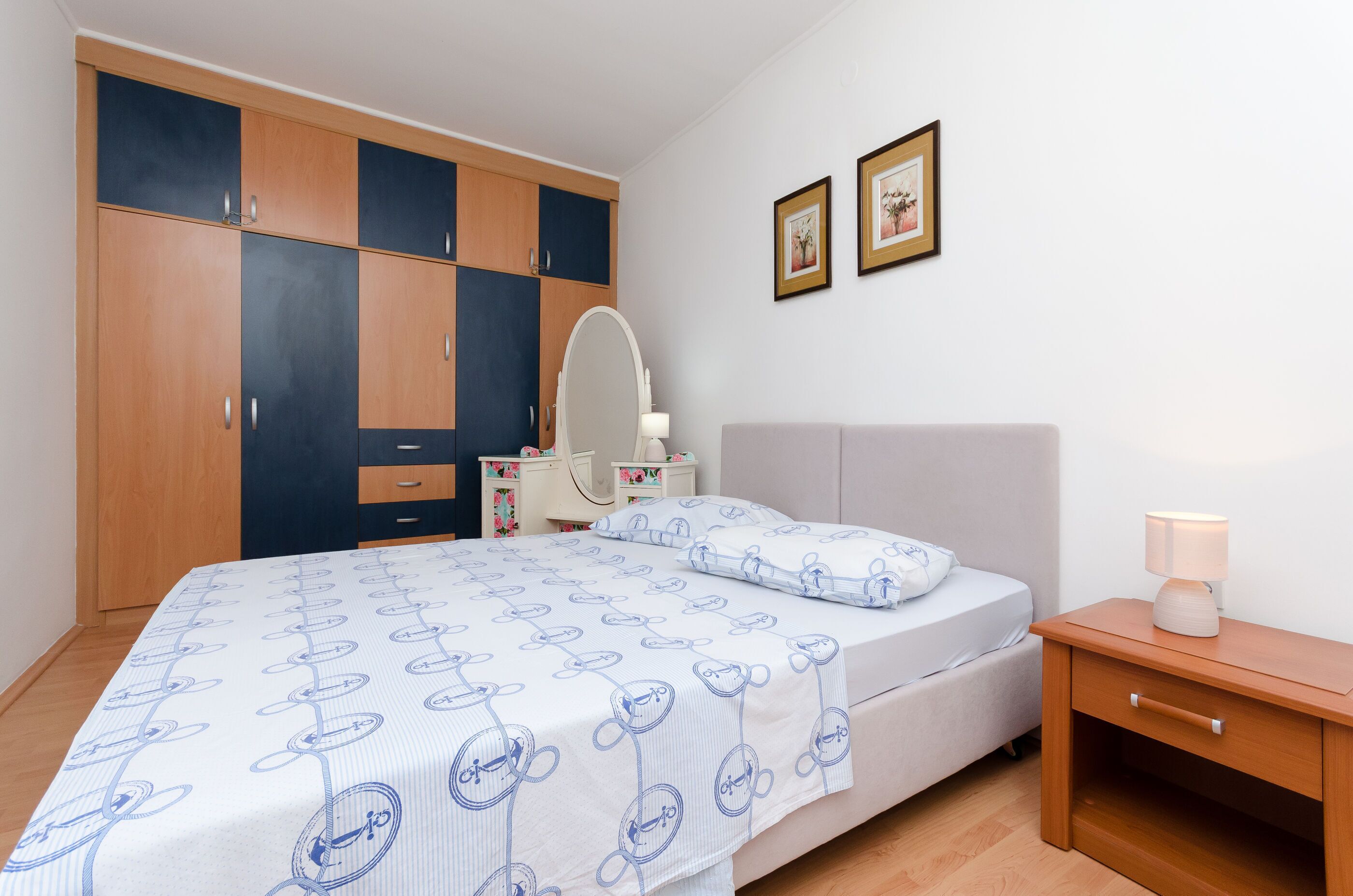 Une chambre à coucher comprenant un lit, une table de chevet, une commode, un miroir et deux tableaux encadrés accrochés au mur.