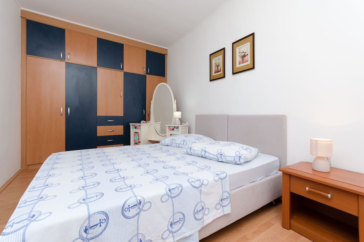 Un dormitorio con una cama, una mesita de noche, un aparador, un espejo y dos cuadros en la pared.
