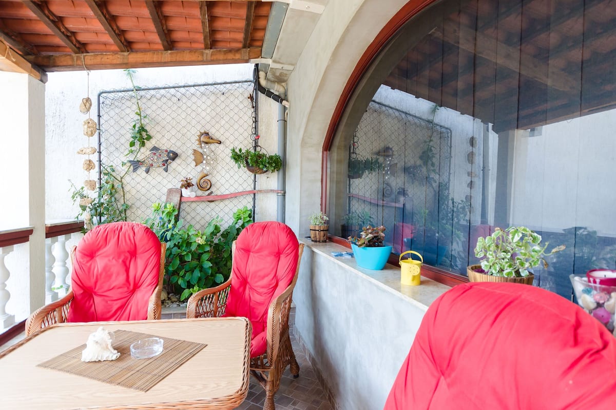 Un balcón con sillas de mimbre, una mesa y plantas en macetas.