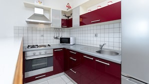 Une cuisine moderne avec des meubles blancs et rouges, une cuisinière en acier inoxydable, un four à micro-ondes et un évier.