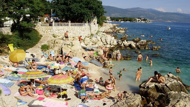 Une plage bondée où l’on voit des gens bronzer, nager et des enfants jouer.