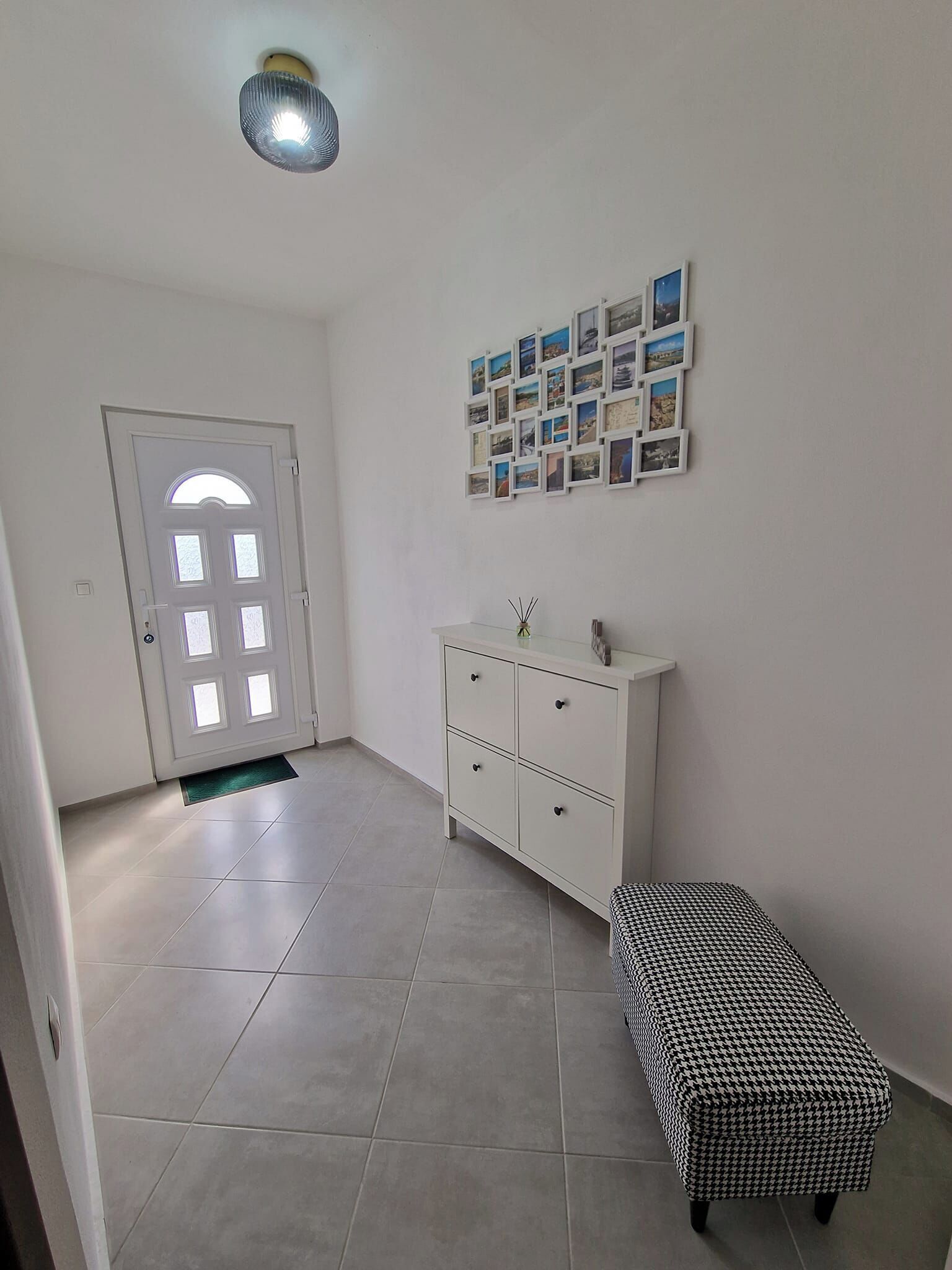A room with a white door, a white cabinet with drawers, a houndstooth bench, and a wall with framed pictures.