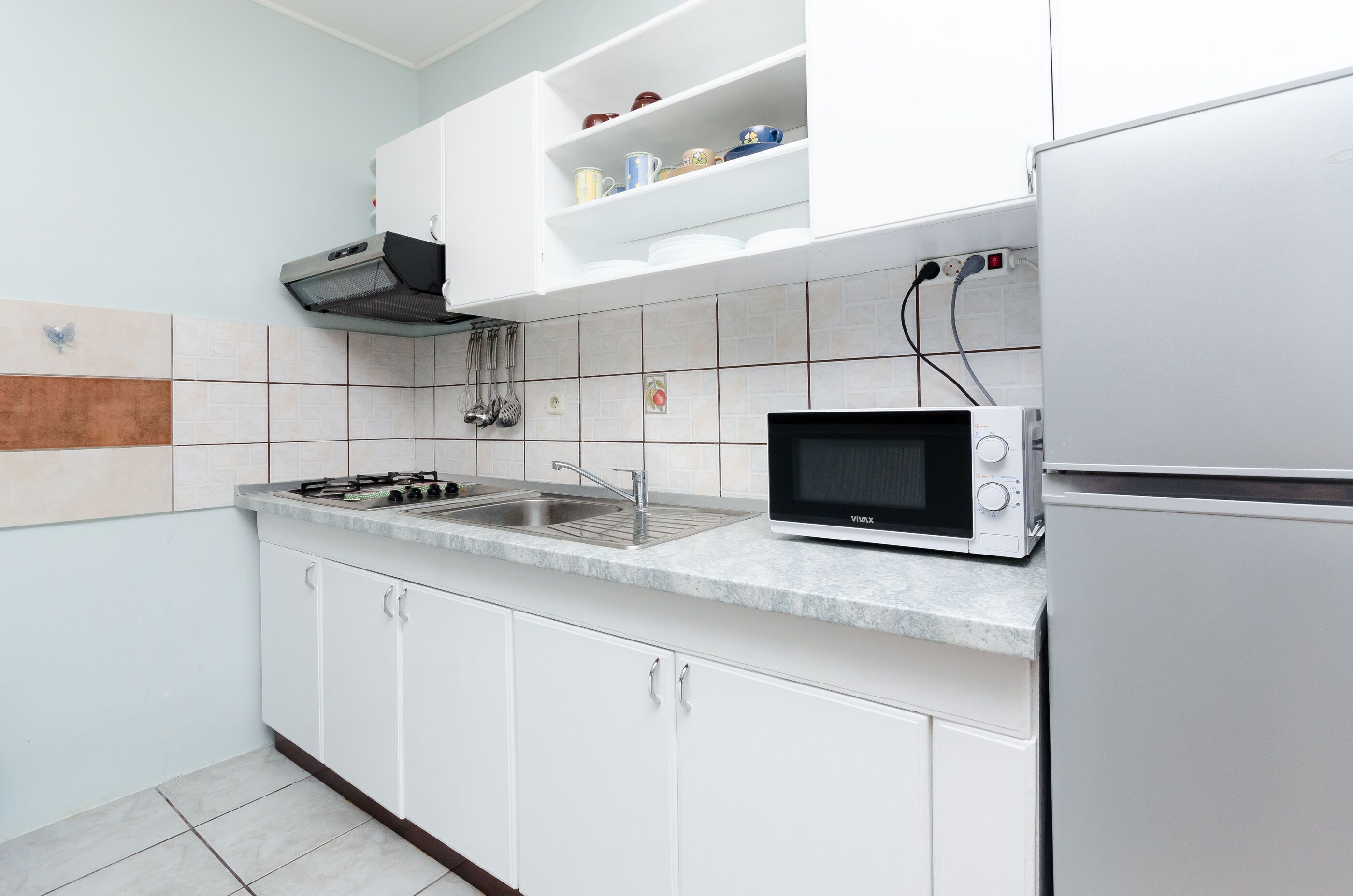 Uma cozinha moderna com armários brancos, fogão a gás, micro-ondas e pia.