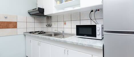 Egy modern konyha fehér szekrényekkel, gáztűzhellyel, mikrohullámú sütővel és mosogatóval.