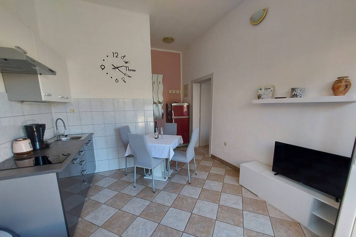 A compact kitchen with a dining area, a TV, and a clock on the wall.