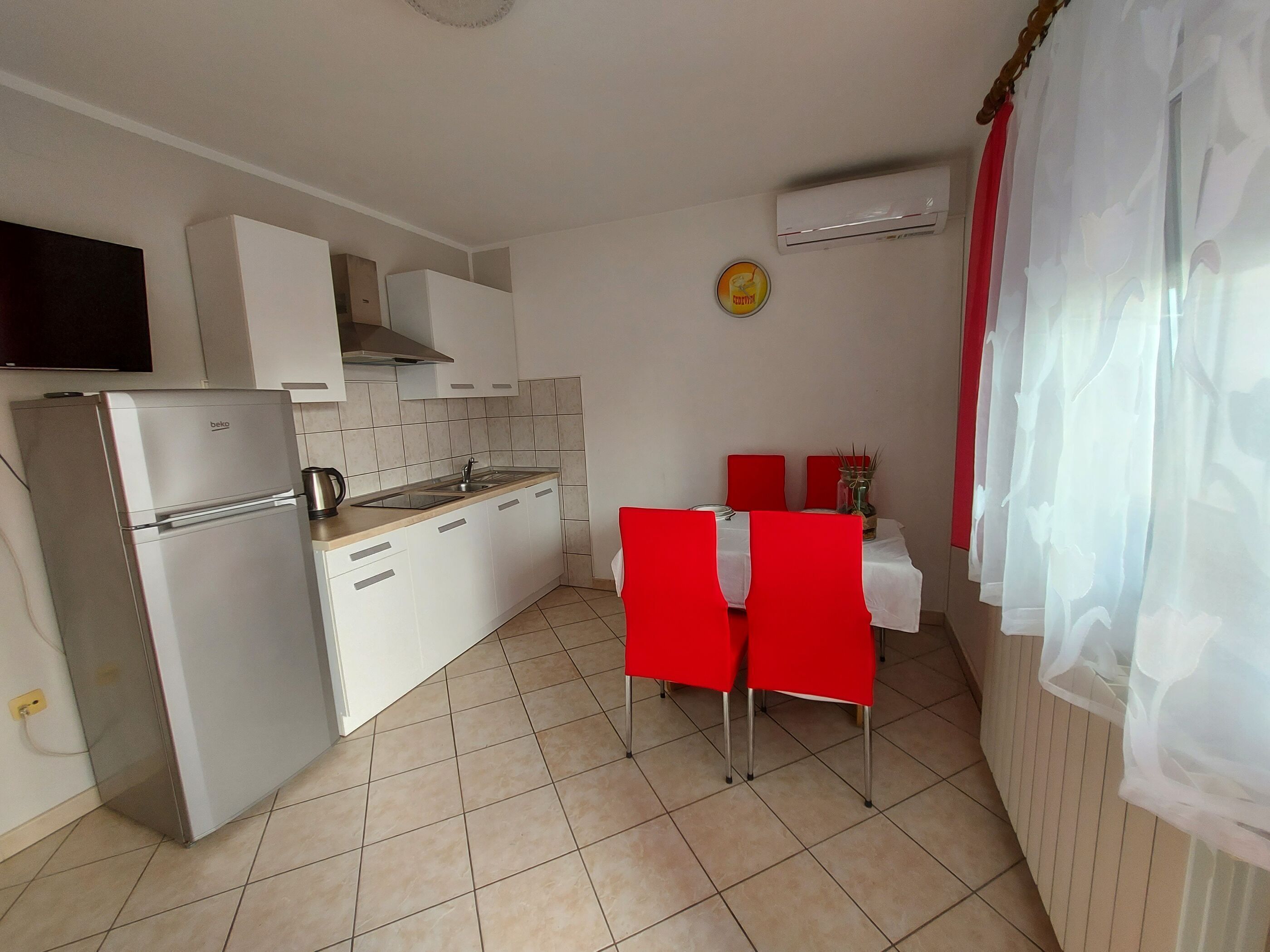 Una cocina compacta con armarios blancos, estufa integrada y un pequeño comedor con sillas rojas y una mesa.
