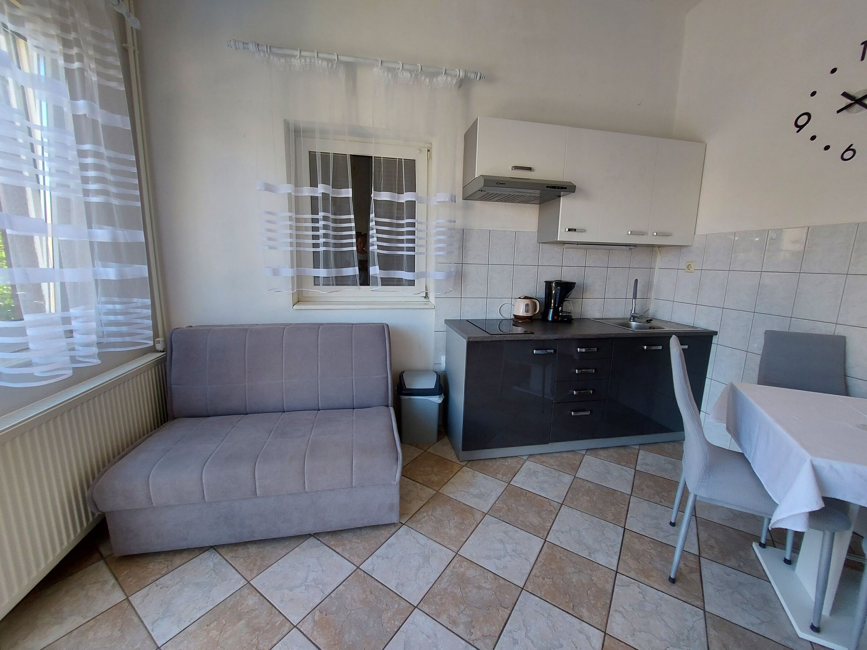 Cocina compacta con sofá, una pequeña mesa de comedor y un ventanal con cortinas translúcidas.