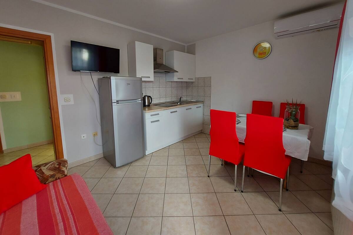 A compact kitchen with white cabinets, a built-in oven, and a flat-screen TV mounted above the counter.