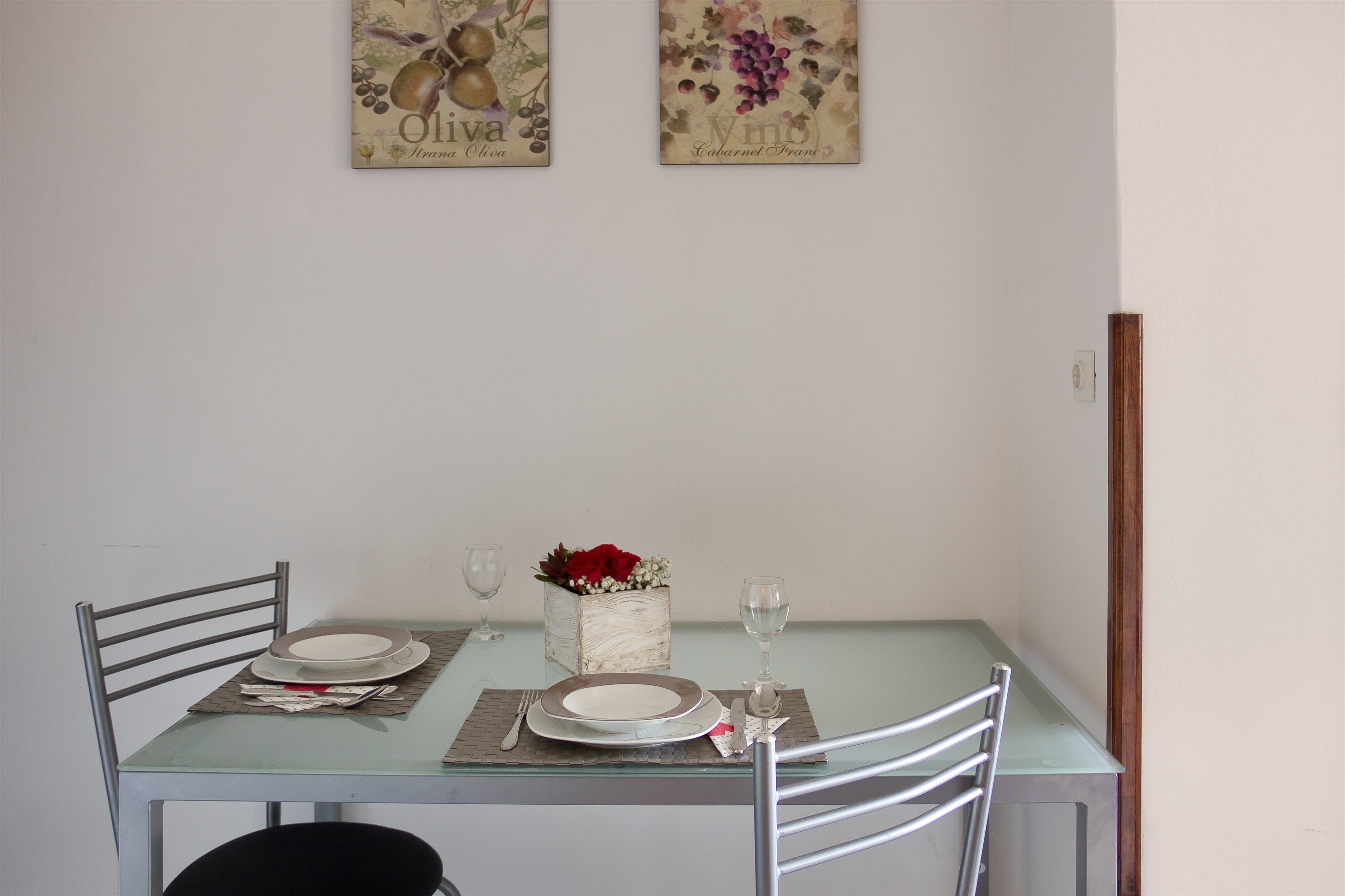 A dining table set with plates, cutlery, and a vase with flowers.
