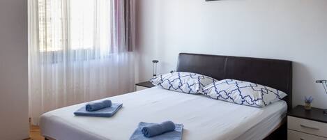 A neatly made bed with blue towels, a dark headboard, and a painting of a lighthouse on the wall.