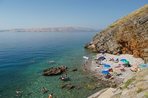 A beach with clear water, rocky shore, and people sunbathing.