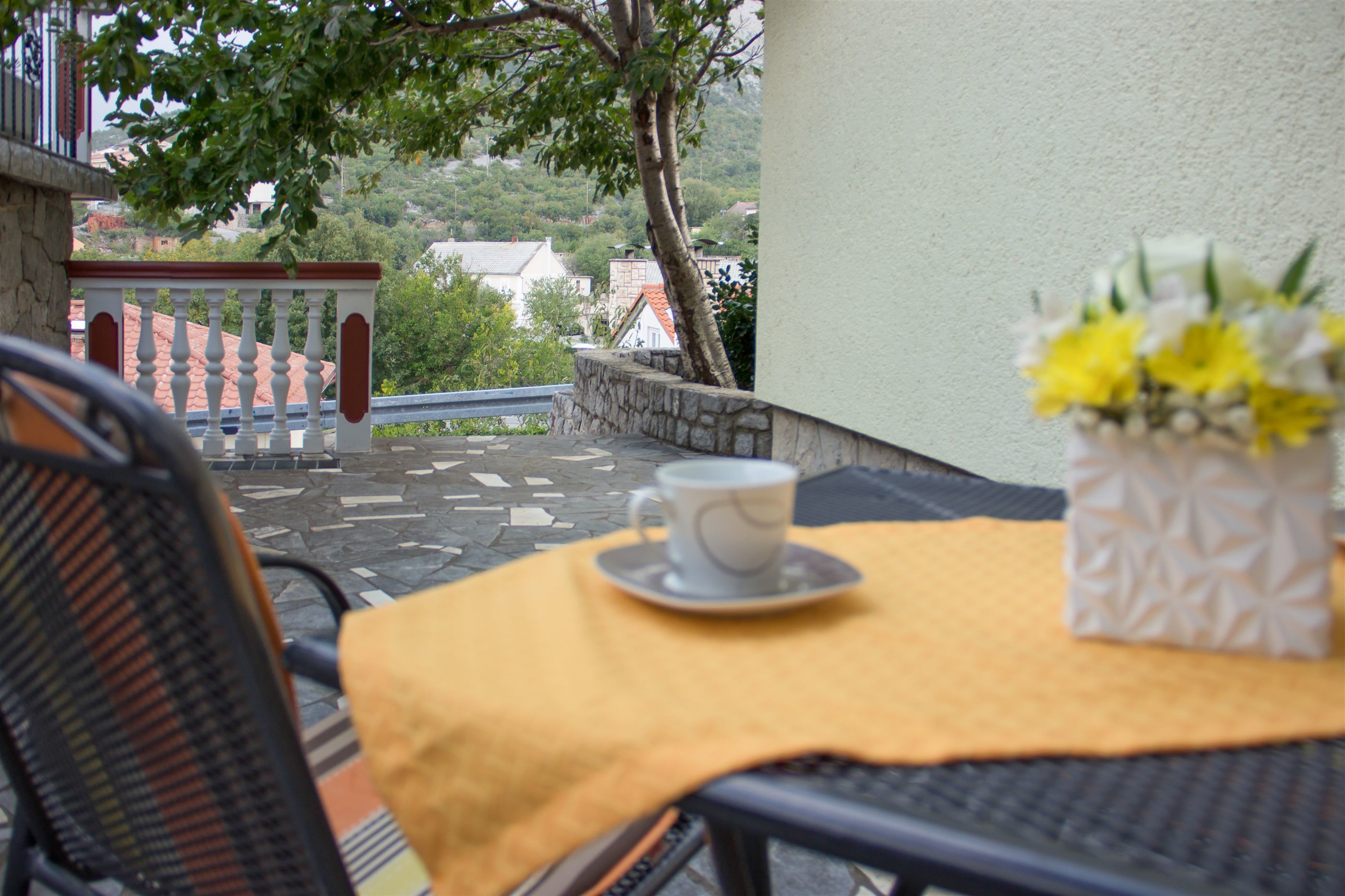 A table with a yellow tablecloth, a white cup, and a vase with yellow flowers.