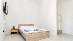 A minimalist bedroom with a wooden bed, a nightstand, a TV mounted on the wall, and a wardrobe. - Apartments Brulo (Razanj)