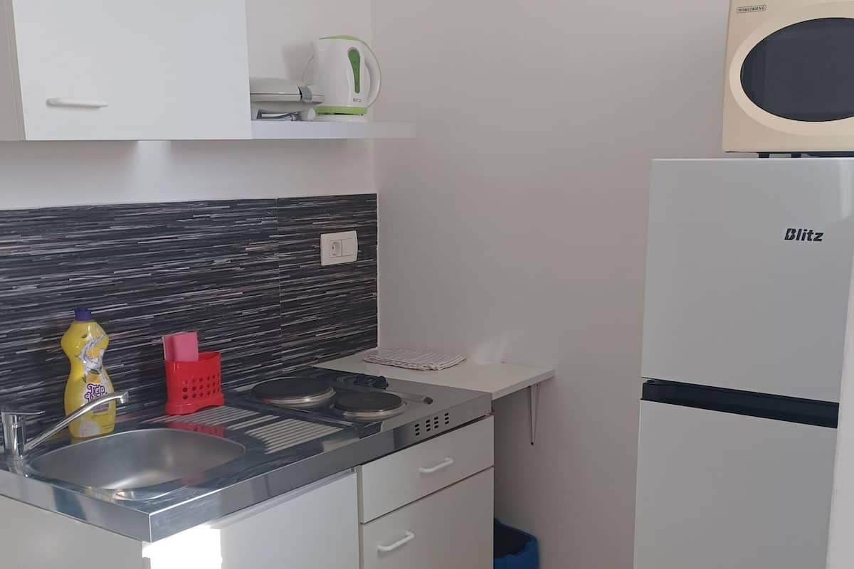 A compact kitchen with a modern design, featuring a sink, a kettle, a toaster, and a refrigerator.