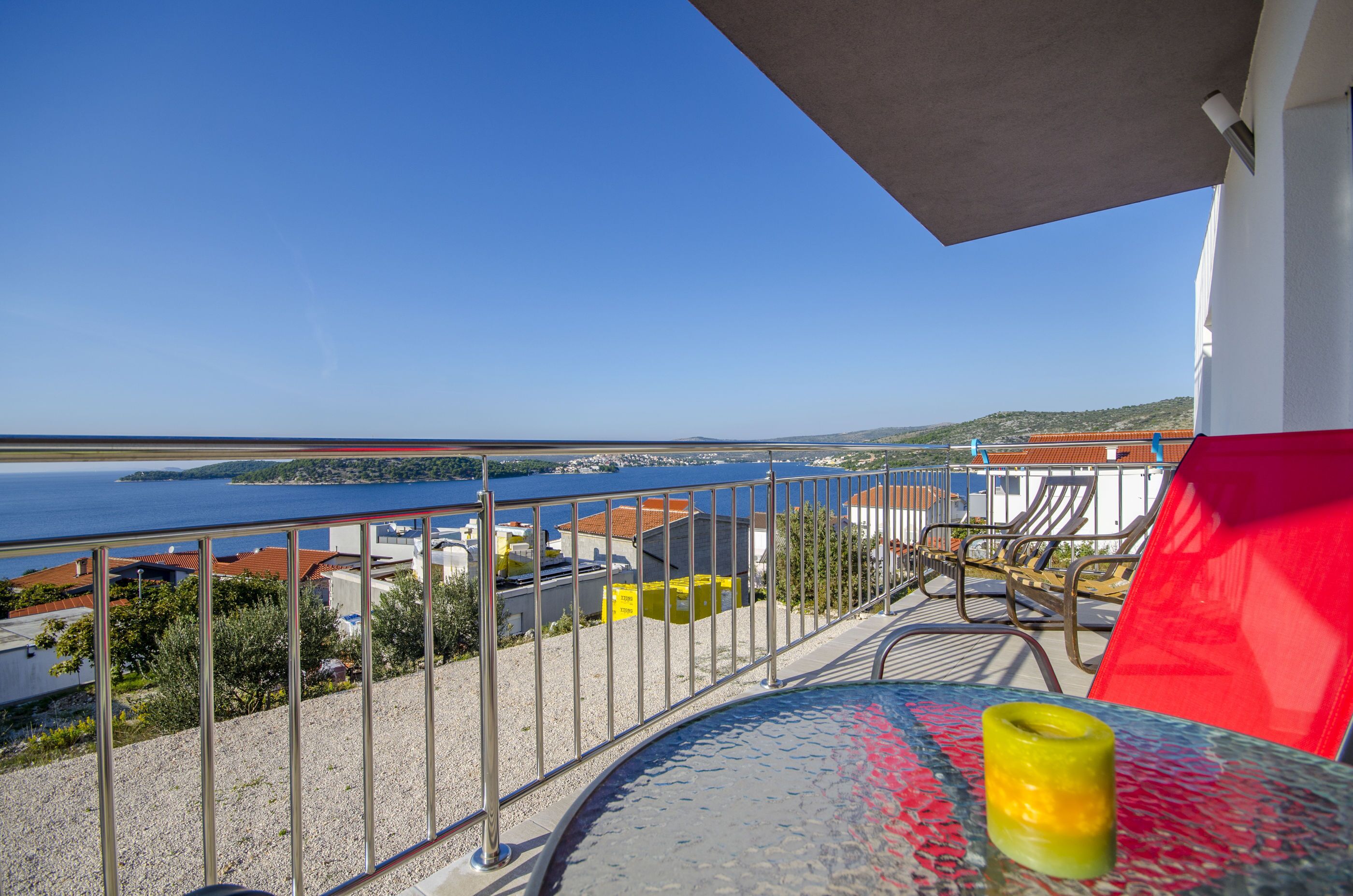 Ein Balkon mit Blick auf das Meer, ein Tisch mit Glasplatte und ein gelbes Kerzenlicht.