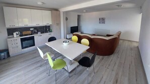 A modern kitchen with white cabinets, a dining area with a white table and chairs, and a cozy seating area with a brown sofa and cushions. - Apartments Brulo (Razanj)