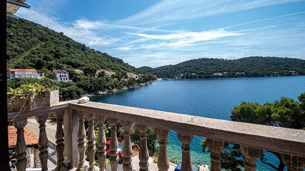A balcony with a view of a lake, surrounded by greenery and buildings. - Apartments Mila (Ubli)