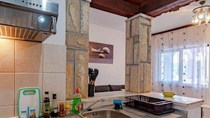 A kitchen with a stone backsplash, a built-in dishwasher, and a window with sheer curtains. - Apartments Mila (Ubli)