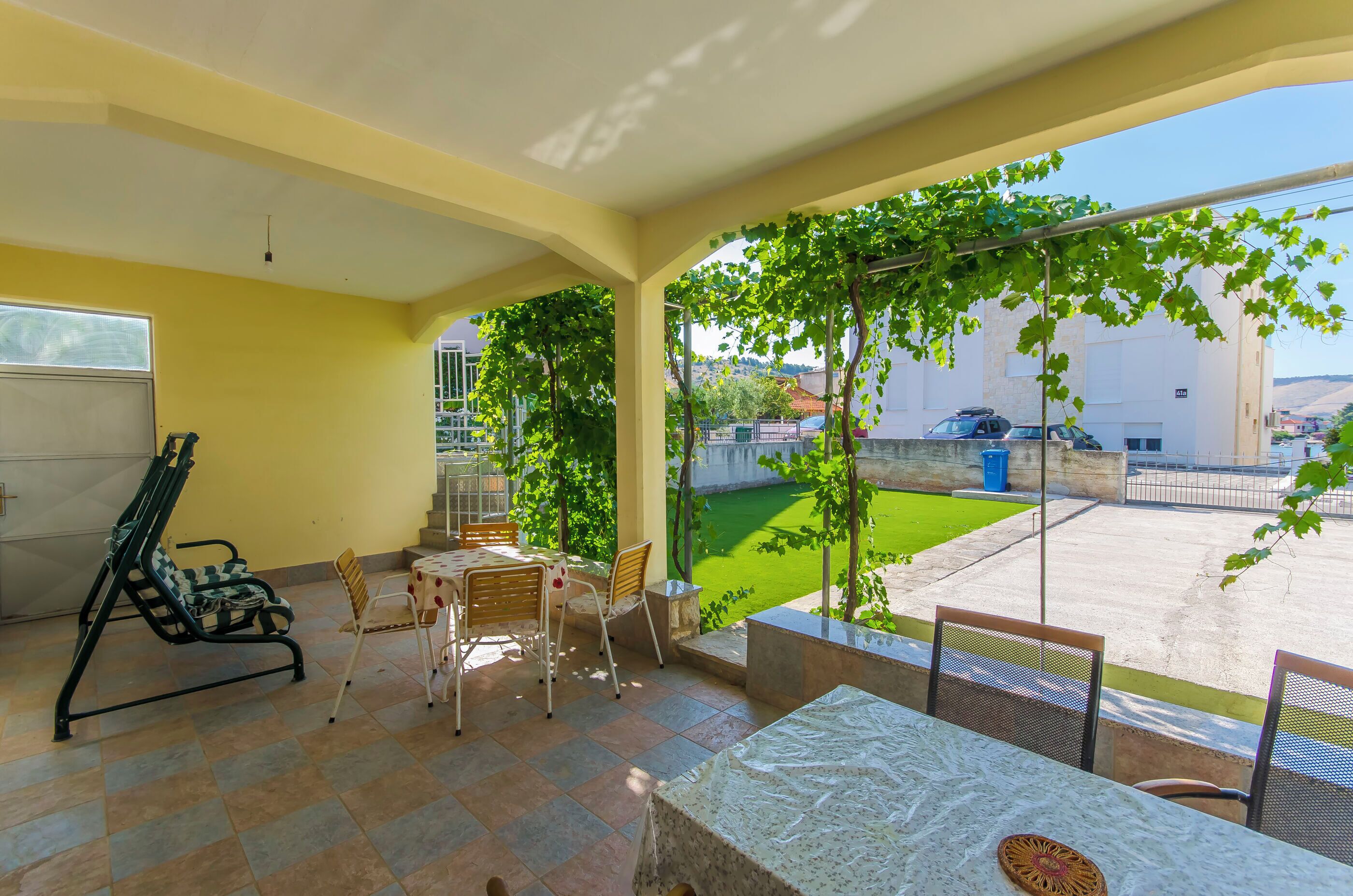 Un patio con una mesa y sillas, una silla plegable, y vistas a un césped verde y edificios.