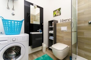 A compact bathroom with a washing machine, a sink, a toilet, and a shower area. - Apartments and Room Gabriels Paradise (Kastel Luksic)