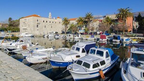 A marina with several boats docked, a historic building with a red roof, and palm trees in the background. - Apartments and Room Gabriels Paradise (Kastel Luksic)