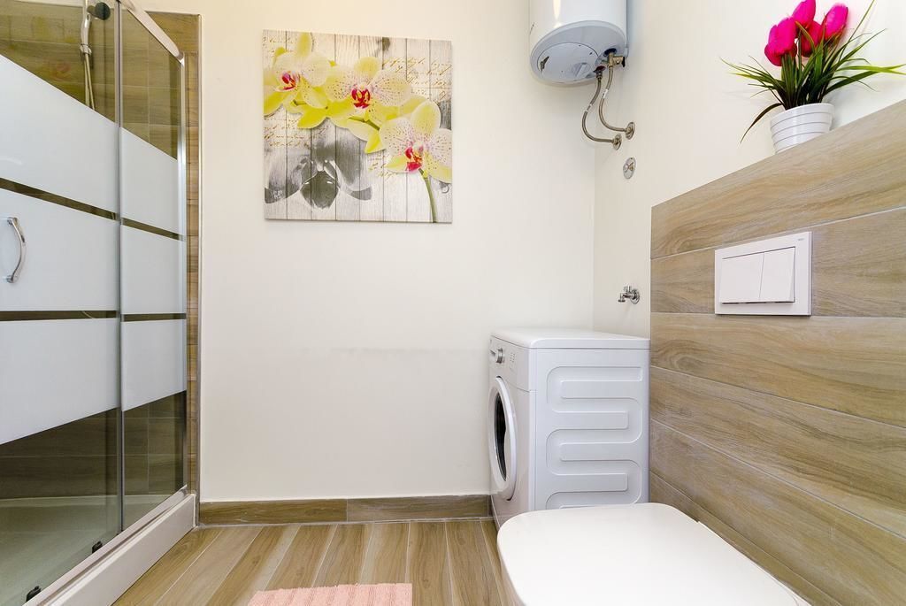 A bathroom with a glass shower enclosure, a washing machine, a toilet, and a wooden vanity.