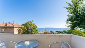 Ein Balkon mit zwei Metallstühlen und einem Glastisch, mit Blick auf ein Gewässer und ferne Hügel.