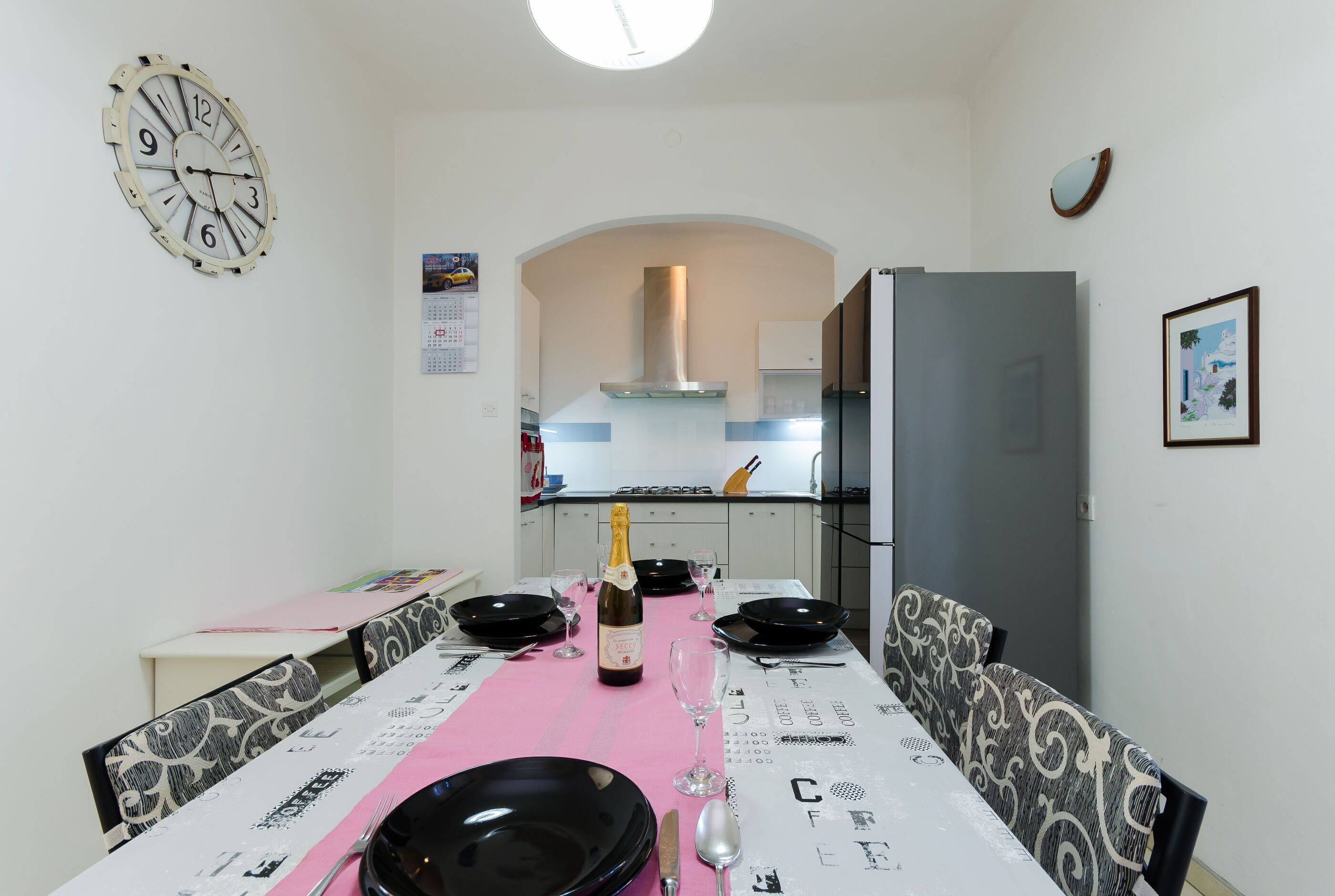 Un comedor con una mesa preparada para cuatro personas, una botella de champán y un reloj en la pared.