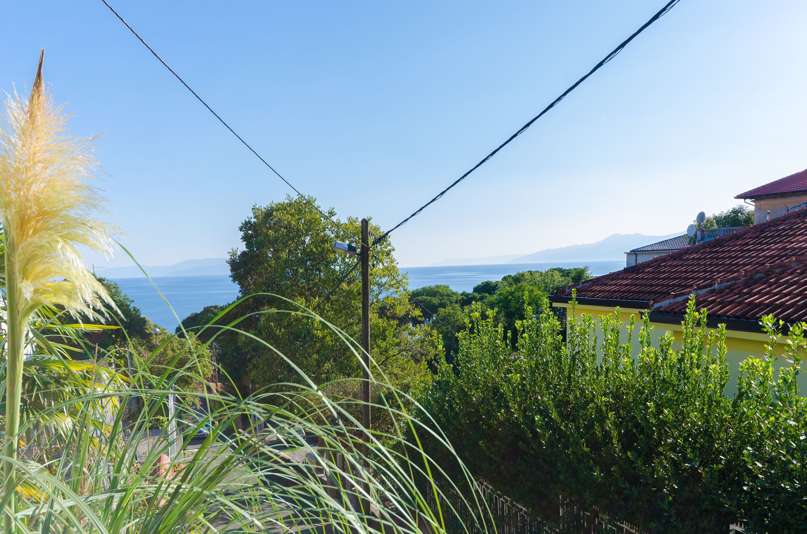 A coastal view with a clear sky, vegetation, and a building with a red roof.