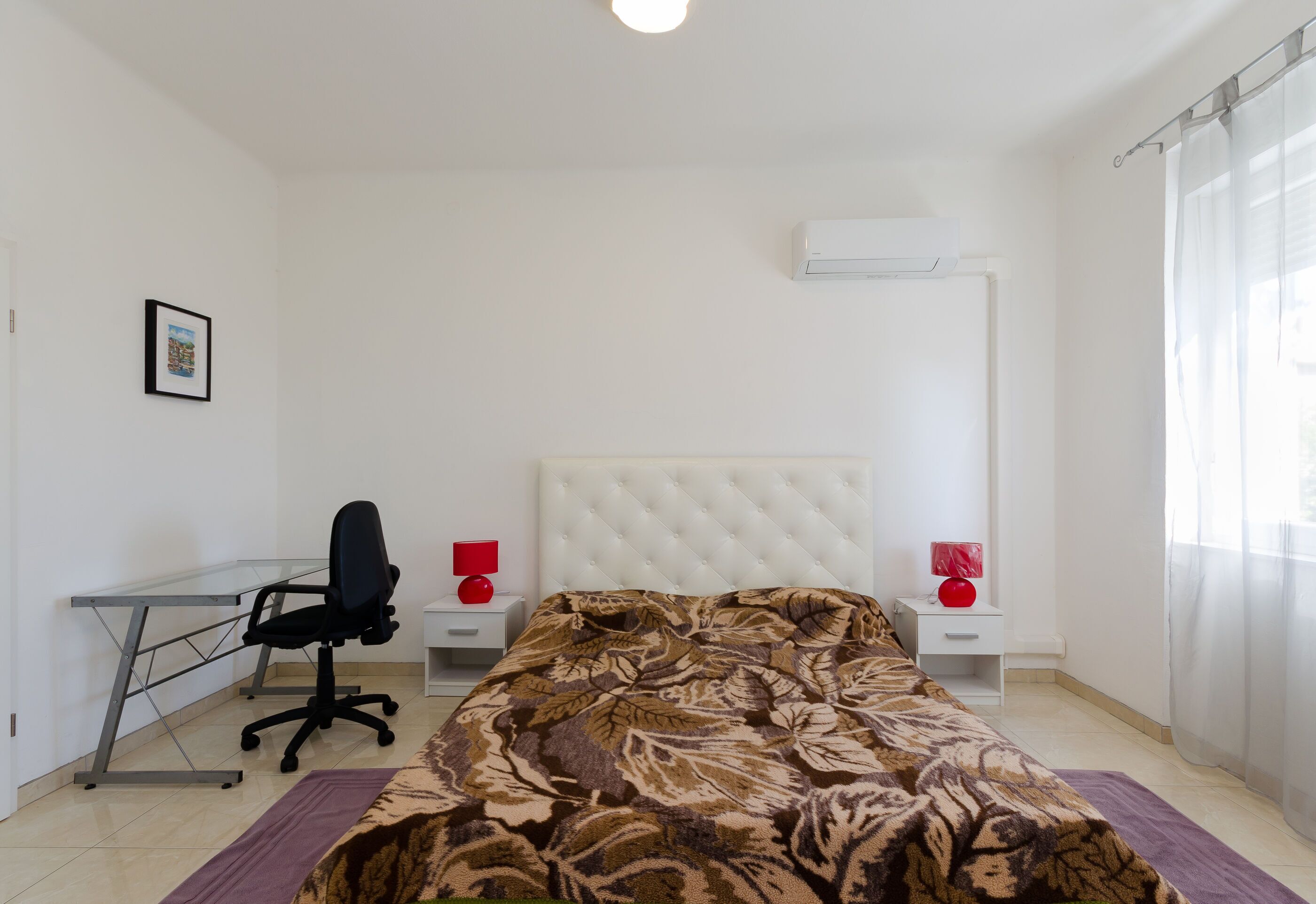 A bedroom with a bed, a desk, a chair, and a window with curtains.