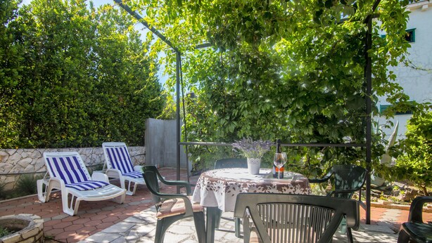 Patio esterno con tavolo e sedie, immerso nel verde e delimitato da un muro in pietra.