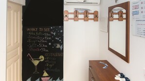 Un’area reception con una lavagna che mostra un messaggio di benvenuto e un elenco di attrazioni. Si nota un armadietto in legno e uno specchio appesi al muro.