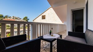 A balcony with wicker furniture, a table with a bottle, and a view of a building with a sloped roof. - Apartment Loro (Ploce)