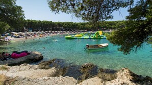 Ein Strand mit klarem türkisblauem Wasser, einer felsigen Küste und einem Boot im Wasser.