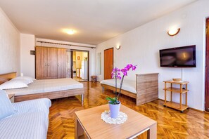 A hotel room with a bed, a sofa, a TV, a small table with a plant, and a wooden floor.