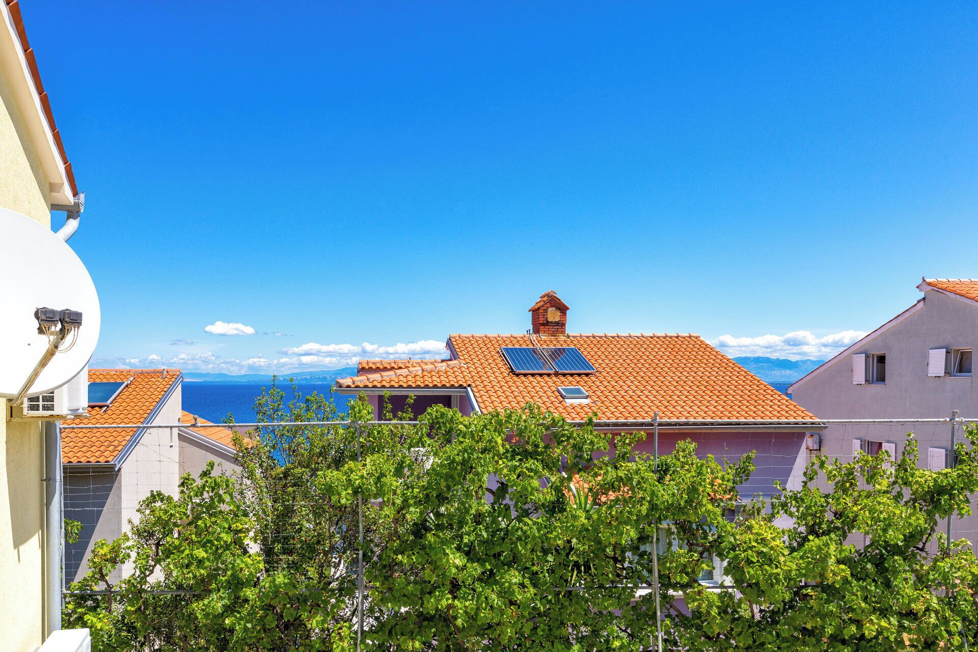Un quartier résidentiel situé sur la côte, caractérisé par des toits recouverts de tuiles en terre cuite, des panneaux solaires et une vue dégagée sur la mer.