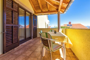 A balcony with a table and chairs, a wooden ceiling, and a view of buildings. - Apartments Arsen (Mali Losinj)