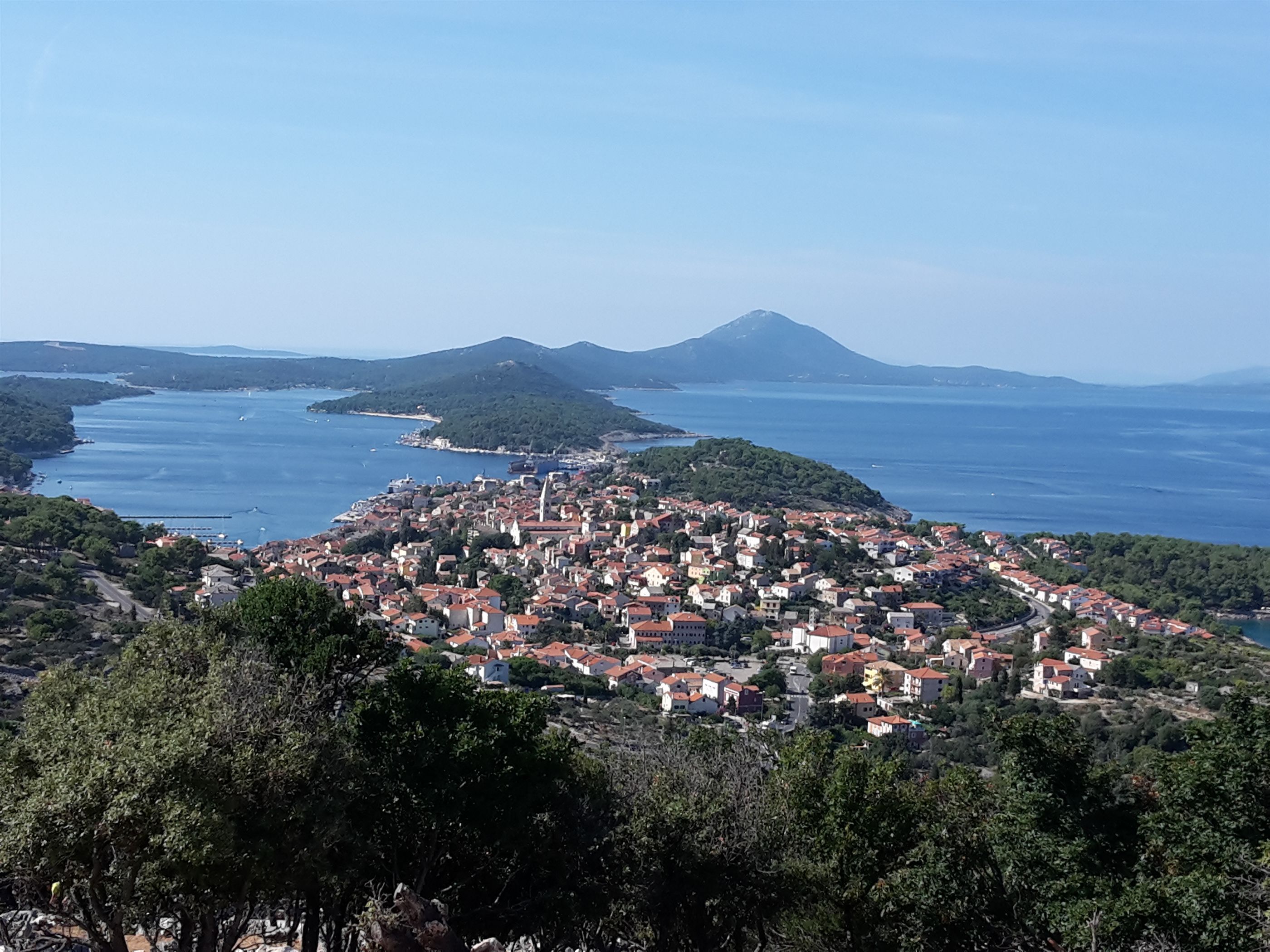 Eine Küstenstadt mit einer dichten Bebauung, einem markanten Berg im Hintergrund und freiem Blick auf das Meer.