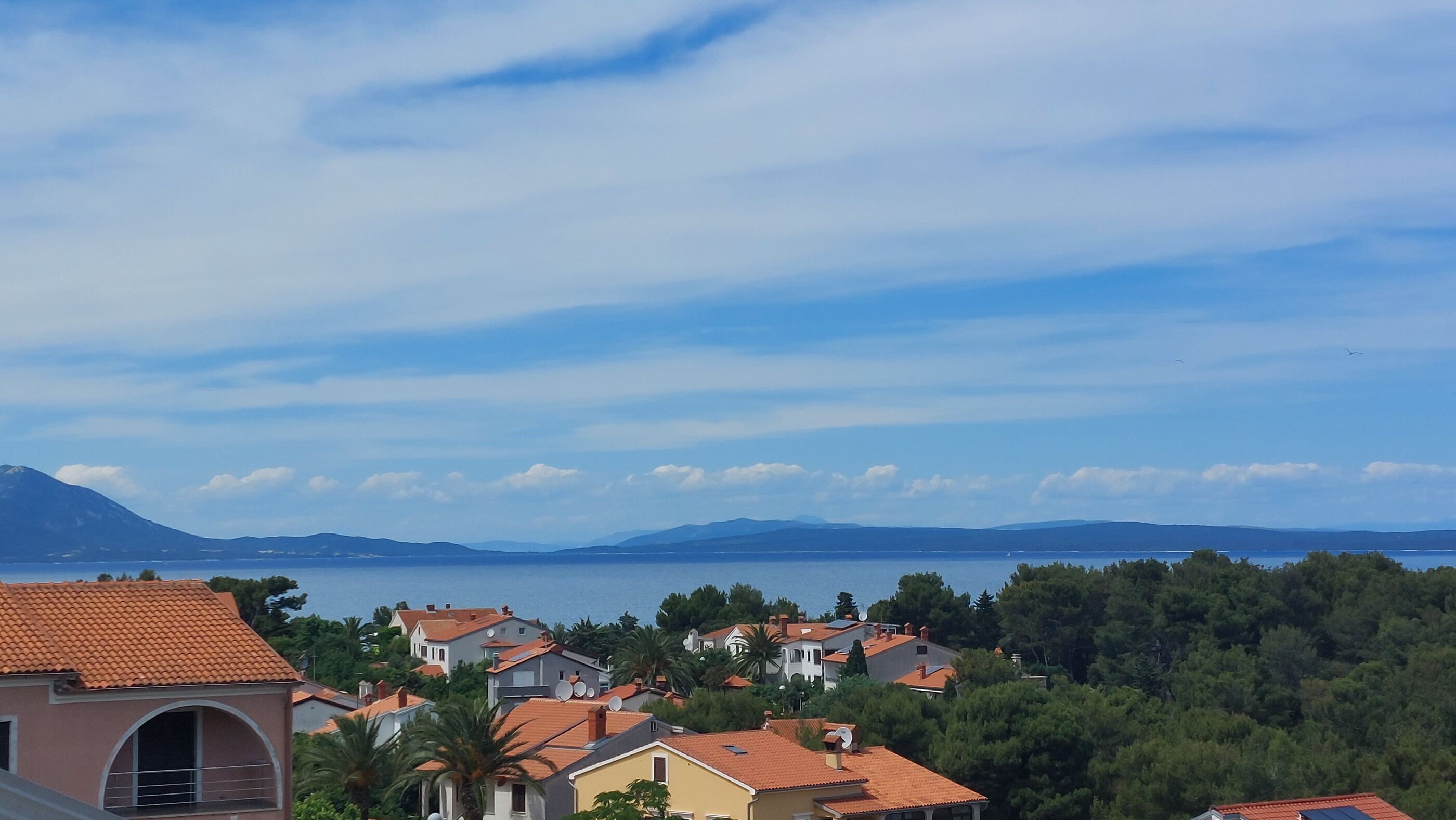 Μια παραθαλάσσια οικιστική περιοχή με σπίτια, καθαρό ουρανό και μια οροσειρά που διακρίνεται στο βάθος.