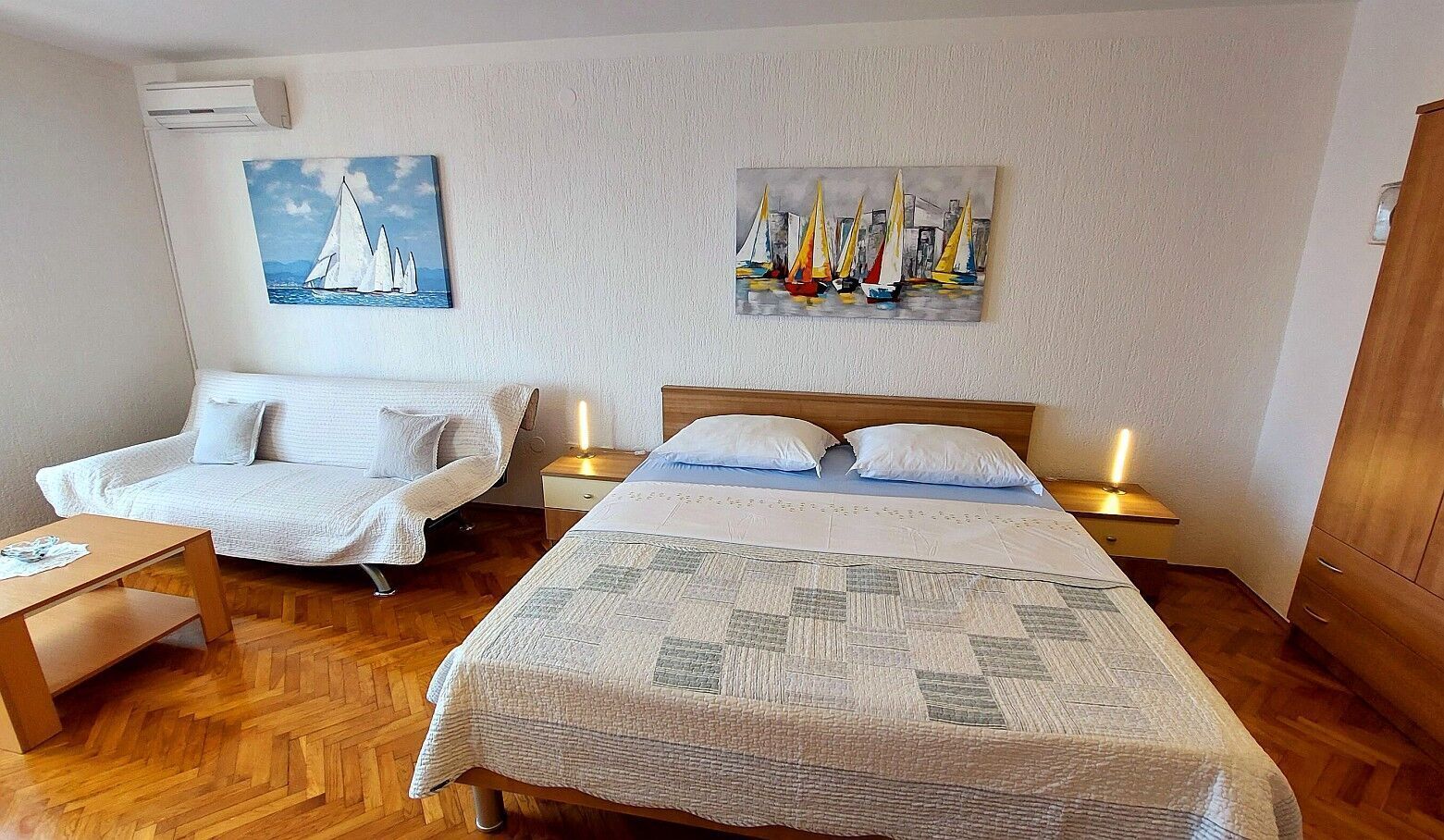 Ein Schlafzimmer mit einem Bett, zwei Nachttischen, einem Sessel, Holzboden und zwei Bildern an der Wand.