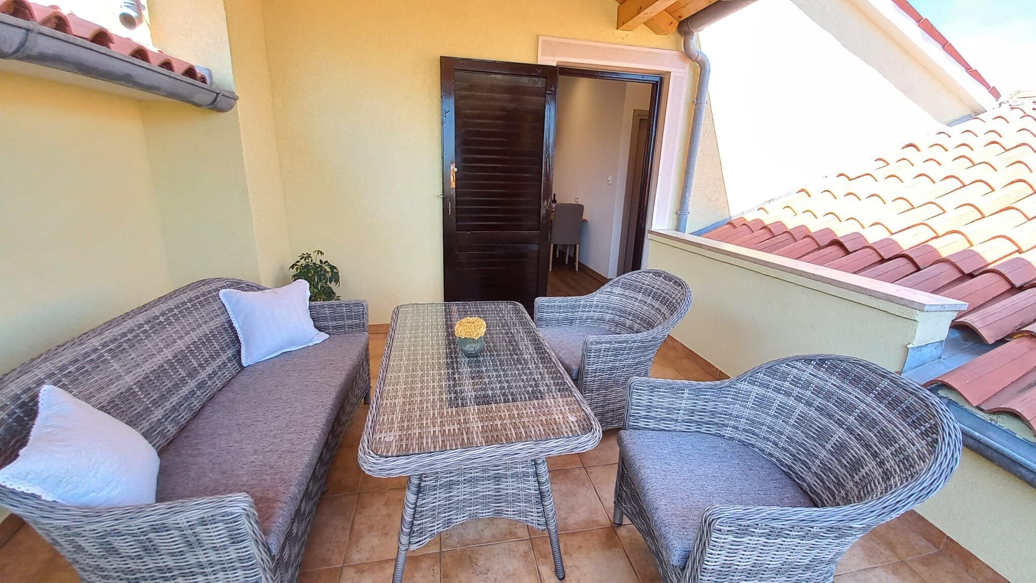 A balcony with wicker furniture, including a sofa and chairs, and a small table with a flower vase.