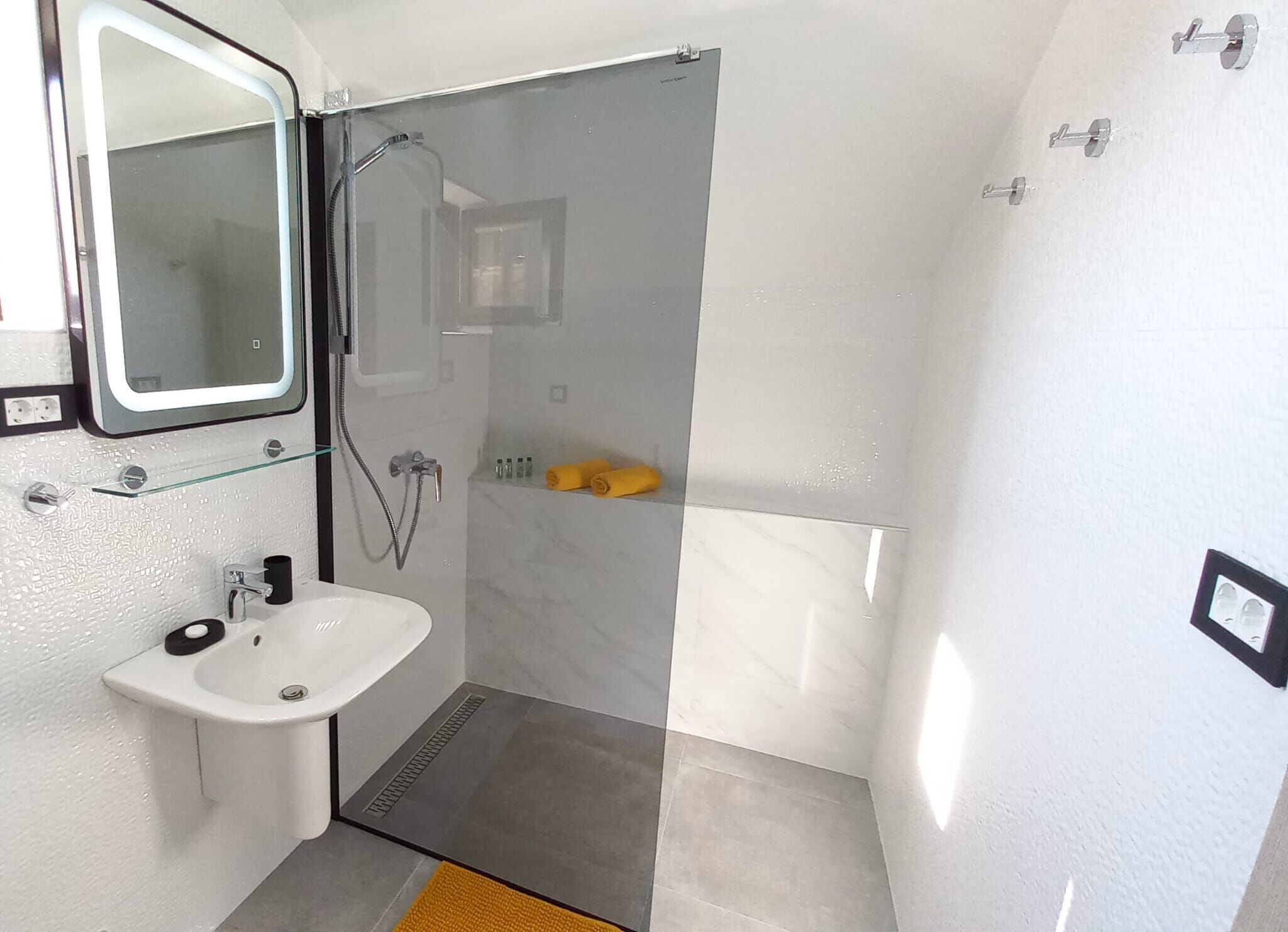 A compact bathroom with a sink, mirror, shower, and towel storage.