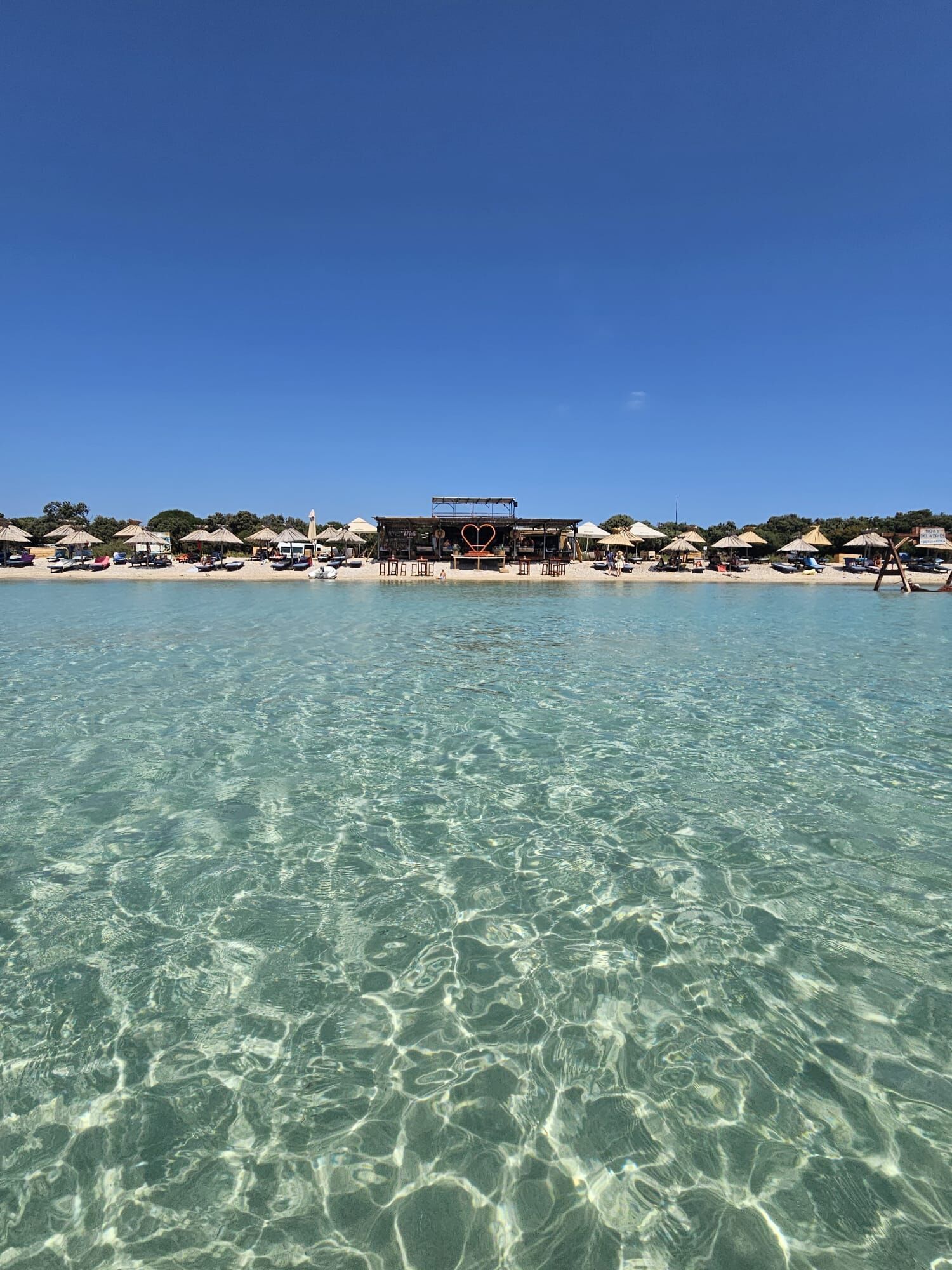 Une plage avec une eau claire, des parasols et un espace bar.