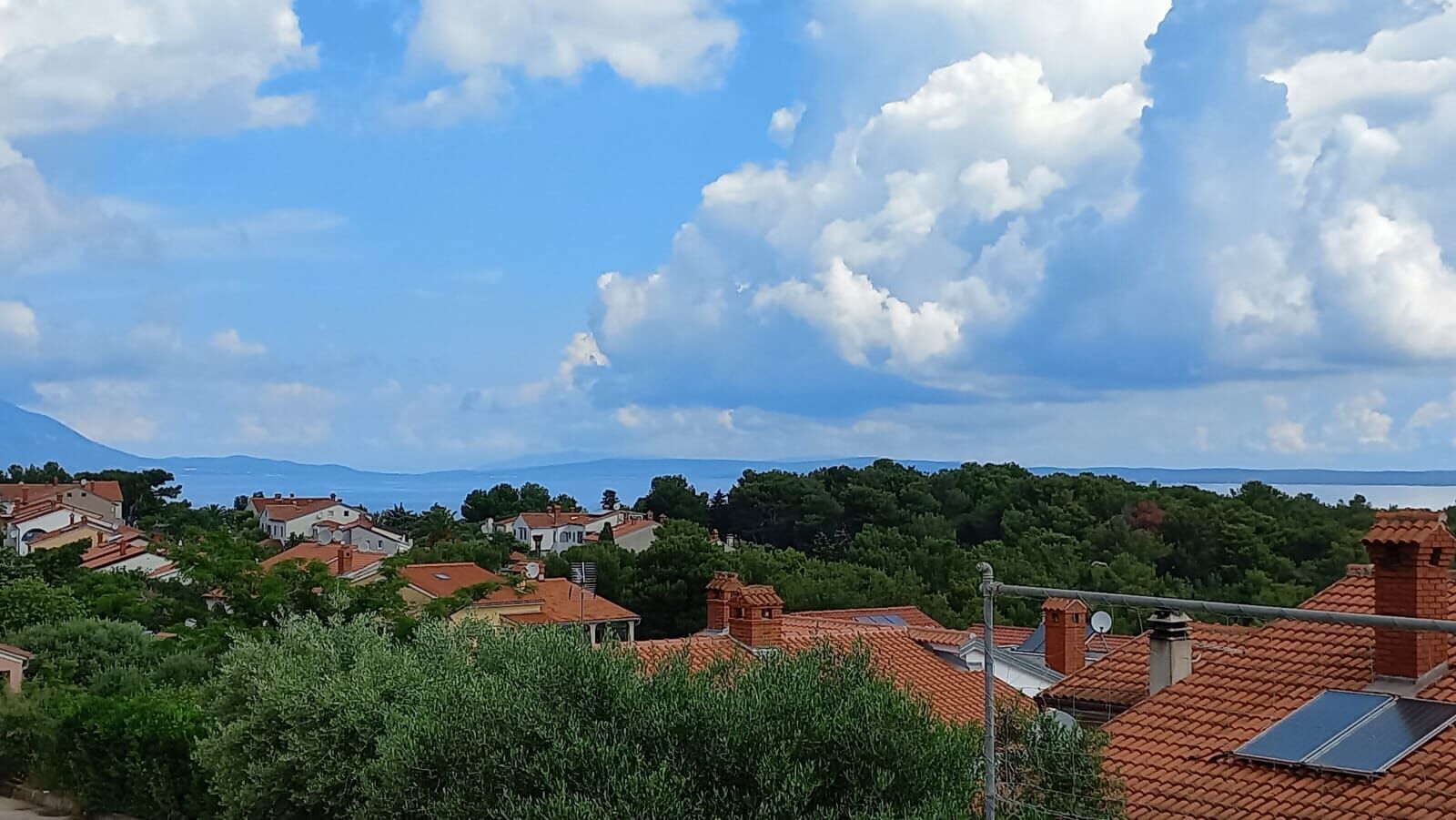 Ett bostadsområde med hus, några med röda tegeltak, och en klar himmel med moln.