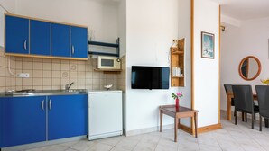 A compact kitchen with blue cabinets, a white refrigerator, a microwave, and a TV mounted on the wall. - Apartment Iva (Banjol)