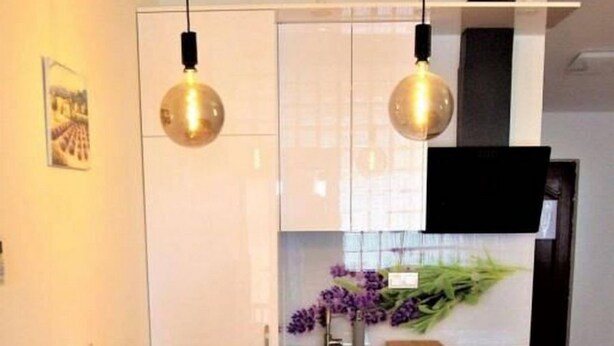 A modern kitchen with white cabinets, two pendant lights, a dining table with chairs, and a vase with purple flowers on the counter. - Apartments Olive i Lavender (Mandre)