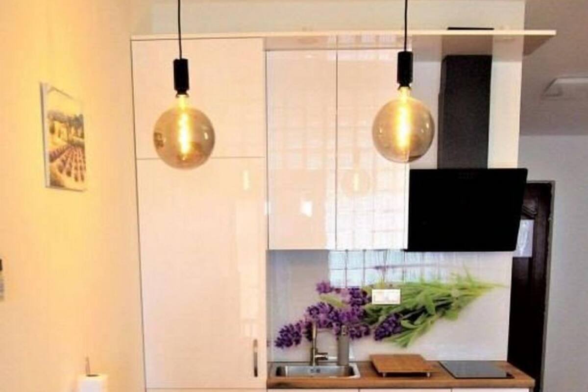 A modern kitchen with white cabinets, two pendant lights, a dining table with chairs, and a vase with purple flowers on the counter.
