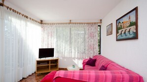 A room with a red sofa, a television on a wooden stand, and a painting on the wall. - Apartments Zorka (Novi Vinodolski)