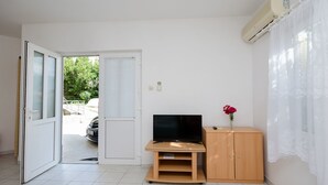 Una habitación con televisión sobre un soporte de madera, un armario pequeño y un equipo de aire acondicionado en la pared.